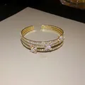 Vista dettagliata di un bracciale rigido dorato a tre strati con fiori in zircone lucenti. - Oro