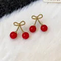 Close-up of red cherry earrings with gold bow detail on white faux fur background - Gold