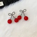 Close-up of elegant red cherry earrings with silver bow details on white fur background - Silver