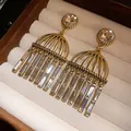 Close-up of gold-toned birdcage tassel earrings with clear zircon stones in a box. - Gold