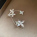 Gros plan détaillé d'un élégant ear cuff fleur en argent avec des strass verts brillants - Style de Boucle d'Oreille Fleur / Argent