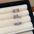 Dettaglio di tre anelli d'argento con pietre rosa a cuore e design a fiocco in una scatola. - Stile Aperto Cuore Fiocco / Argento-Rosa