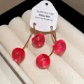 Close-up of red cherry resin drop earrings with gold-toned hooks and product tag (83 chars) - Gold / Pink