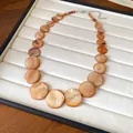 Detailed macro view of bohemian orange shell bead necklace on a jewelry display tray. - Brown