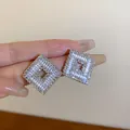Close-up of square silver-toned stud earrings with sparkling cubic zirconia stones - Geometric Square Style