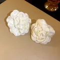 Nahaufnahme von weißen Satin-Kamellien-Stoffblumen auf beigem Lederhintergrund - 925 Sterling Silber Ohrstecker / Weiß