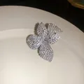 Primer plano de un pendiente de clip con forma de flor y pedrería sobre un plato blanco - Anillo de Flores / Plateado