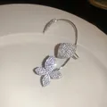 Primer plano de un pendiente trepador de mariposa brillante con pedrería de cristal. - Ear Cuff Oreja Izquierda / Plateado