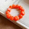 Close-up of orange marbled acrylic geometric beaded bracelet on a textured book surface. - Orange