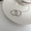Dettaglio ravvicinato di orecchini a cerchio in argento su un piattino di ceramica - Clip per Orecchio Lucida Chiusa Minimalista (26#) / Argento