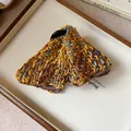Close-up view of a stylish brown checkered tweed triangle hair claw clip on a tray. - Hair Claw / Yellow