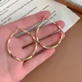 Close-up view of large golden twisted hoop earrings with minimalist spiral design. - Gold