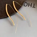 Close-up detail of sleek gold-finish long hook earrings on a textured background. - Gold