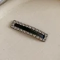 Detailed close-up of a black rectangular hair clip embellished with sparkling rhinestones - White