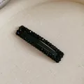Macro detail of a black rectangular hair clip adorned with shimmering rhinestones on fabric - Black