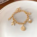 Détail du bracelet doré thème océan avec breloques étoile de mer, coquillage et perle. - Or