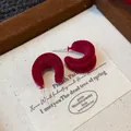 Primo piano di orecchini a lobo rossi floccati a forma di C con trama vellutata - Rosso
