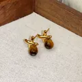 Primo piano di eleganti orecchini a lobo in occhio di tigre dorati dall'estetica vintage - Stile Forma X Incrociata (HE29419)