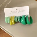 Dettaglio di vari orecchini a cerchio in acrilico verde e giallo su carta da gioielli. - Verde
