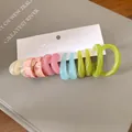 Dettaglio di orecchini a cerchio in acrilico colorato su cartoncino bianco. - Rosa e Verde