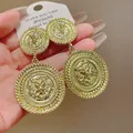 Close-up of golden circular earrings featuring intricate lion head relief design. - Round Lion Head Relief / Gold
