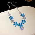 Exquisite detail of a sparkling blue and clear zircon flower necklace on a white tray - Necklace / Silver-Blue