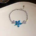 Makroaufnahme eines Armbands mit blauen Zirkonia-Blumen auf einer weißen Schale - Armband / Silber-Blau
