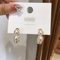 Close-up of elegant C-shaped pearl drop earrings on white display card with gold accents. - Geometric C-Shape (HE3942) / White
