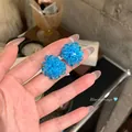 Hand hält funkelnde blaue Blumen-Ohrstecker mit Silbernadeln. - Blauer Perlen-Gewebter Stil (18#)