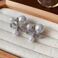 Primo piano di eleganti orecchini a fiocco con perle finte bianche su espositore - 2 modi di indossare / Argento