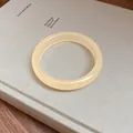 Close-up of a minimalist round resin bangle in creamy yellow on a textured book cover - Beige