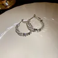 Close-up detail of silver-tone hoop earrings featuring sparkling zircons and polished metal discs - Silver