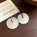 Nahaufnahme von silberfarbenen runden Ohrringen mit Spiralstruktur und Vintage-Design. - Silber