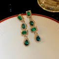 Dettaglio di orecchini retrò con cristalli verde smeraldo, placcatura in oro e strass luccicanti - Verde / Oro