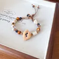 Detailed view of the textured ceramic animal charm and tiger's eye beads on a wax cord - Brown