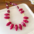 Close-up detail of a marbled magenta acrylic irregular oval bead necklace on a beige tray - Rose Red Smudge