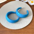Detail view of bold blue acrylic C-shape hoop earrings on a textured display pad - C-Shaped (HE27892) / Blue
