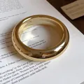 Close-up of a thick minimalist gold-colored bangle on a white magazine background - Thick Glossy Style (5)