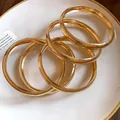Nahaufnahme von minimalistischen goldfarbenen Armreifen auf einem weißen Teller - Polierter Runder Stil (HB4814) / 5 Stück / Gold