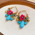 Detailed view of boho woven hoop earrings with red fabric flowers and turquoise stones - Gold-Blue