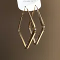 Primo piano dettagliato di eleganti orecchini geometrici a rombo dorati appesi alla carta - Grande / Argento