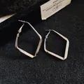 Primo piano dettagliato di orecchini geometrici a rombo color argento su trama nera. - Piccolo / Argento
