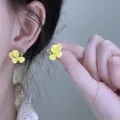 Close-up of sweet yellow flower stud earrings with green leaf detail on model's ear - Style 39 Pink Flamingo