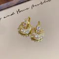 Macro view of gold-plated U-shaped earrings with sparkling cubic zirconia on mirror - U-shaped Bag Design Huggie / Gold