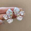 Macro view of elegant flower-shaped earrings with crystal inlay and enamel petals - White