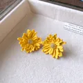 Detailed view of yellow flower stud earrings with sparkling centers on a soft white tray. - Yellow
