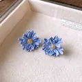 Detailed macro view of matte blue daisy flower earrings with textured golden centers - Blue