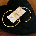 Macro view of minimalist large gold hoop clip-on earrings on black heart velvet stand - Gold