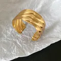 Detailed macro view of a gold metallic wavy textured open cuff bracelet on white paper - Gold