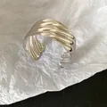 Close-up of a silver-tone metal cuff bracelet featuring bold wave texture details. - Silver